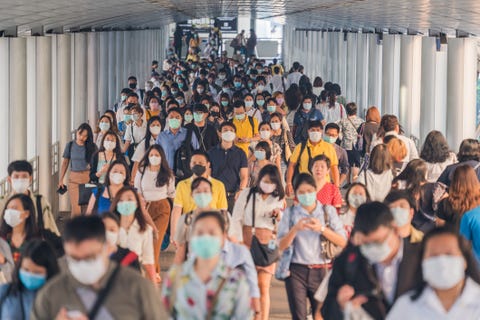 Folle di persone asiatiche che indossano protezioni per il viso mentre si recano al loro posto di lavoro a Bangkok durante le ore di punta mattutine