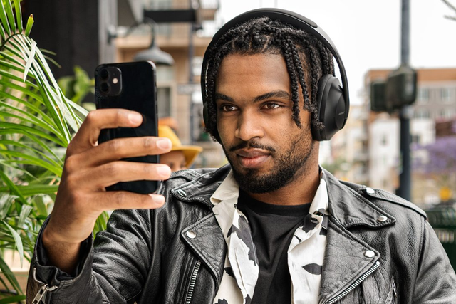 black man in leather jacket holding up cell phone wearing bose 700 headphones
