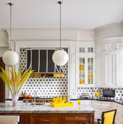 white tiled kitchen with center island with wooden storage beneath and marble top and yellow backed stoolls