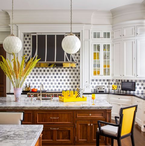 white tiled kitchen with center island with wooden storage beneath and marble top and yellow backed stoolls