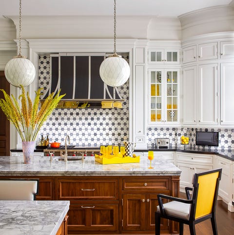 A List 2022 - ELLE DECOR white tiled kitchen with center island with wooden storage beneath and marble top and yellow backed stoolls