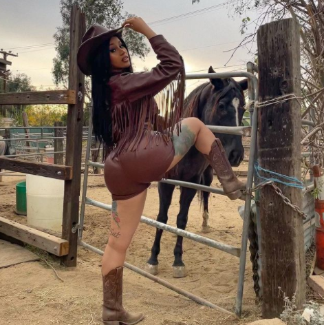 cardi b posando vestida de cowboy delante de un caballo