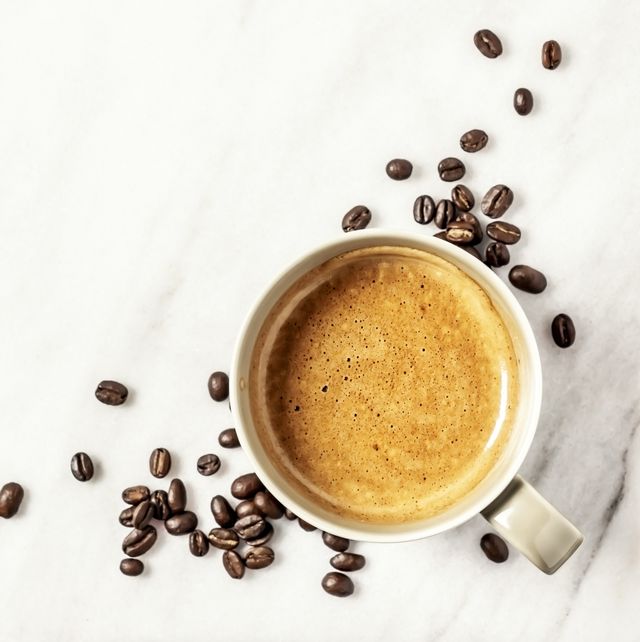 a cup of coffee and coffee beans on white, marble background