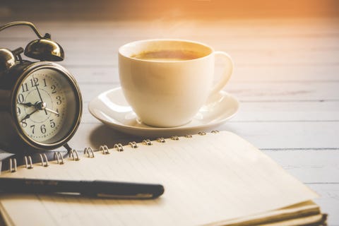 cup of hot coffee ,clock,notebook and pen on wooden table