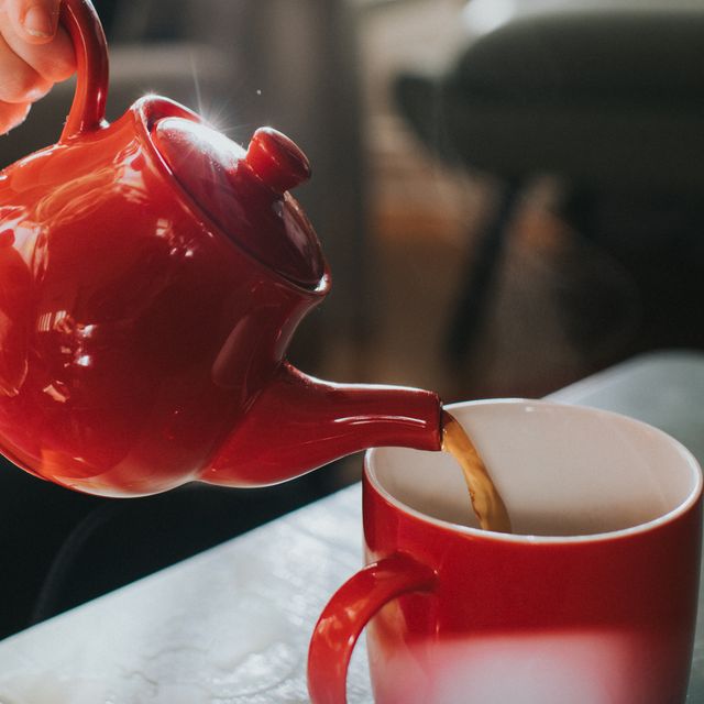 shiny small red ceramic teapot, pouring hot tea into a red mug conceptual with space for copy