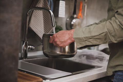 cut out shot of man pouring water from the faucet into a cooking pot