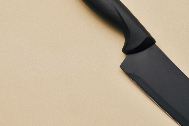 an all black knife on a tan rubber cutting board