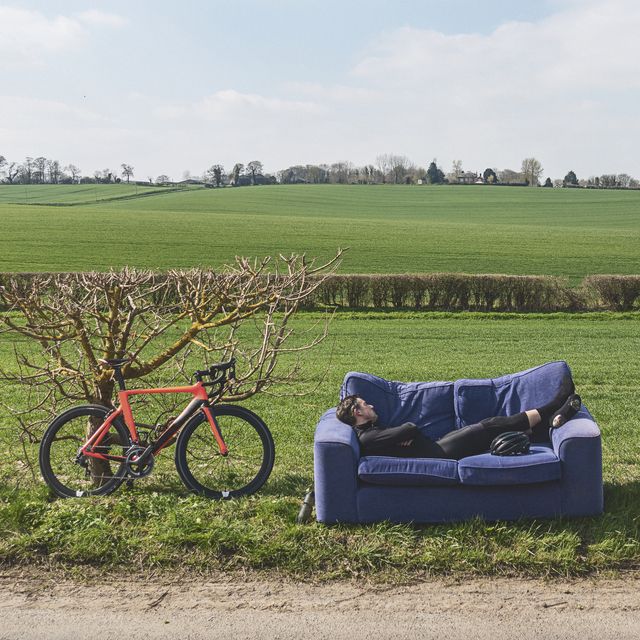 een man ligt buiten op een bank te slapen, naast zijn fiets