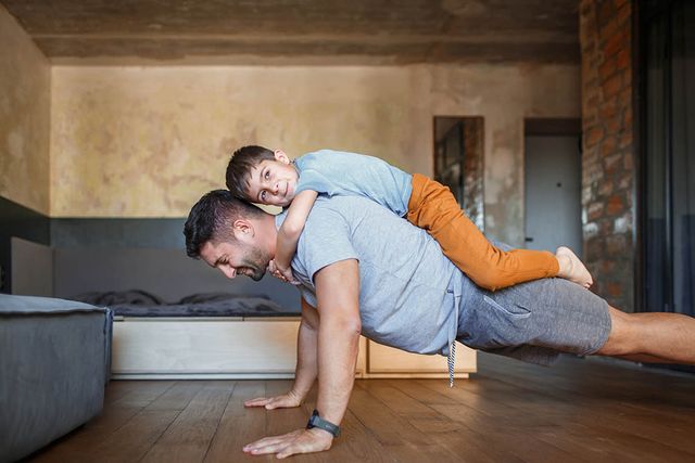 dad does exercises with his son wring out from the floor with a boy on his back the boy hugged his dad's neck and wistfully looks away
