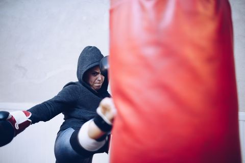 Young female kickboxer kicking punching bag at gym