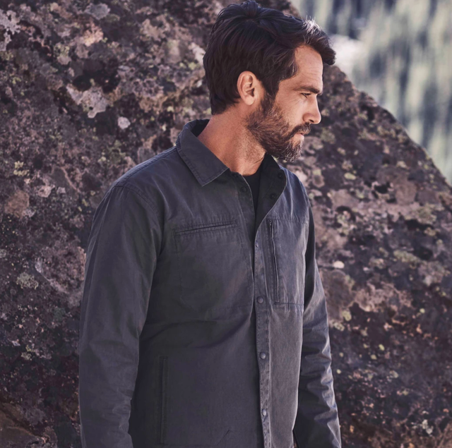 Aether Echo Jacket a model in front of a boulder wearing a graphite jacket