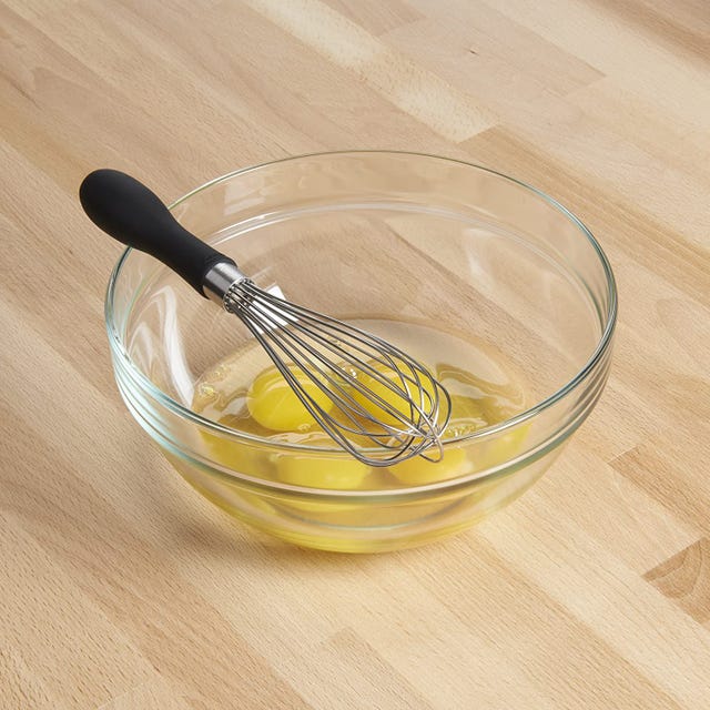 OXO Good Grips 9-Inch Whisk a whisk with a clear bowl with broken egg yolks in it on a wood tabletop