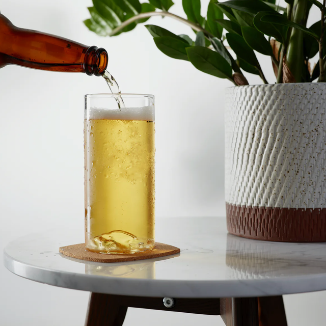 Whiskey Peaks Half Dome Beer Glass a beer bottle being poured into a beer glass on a table with a plant