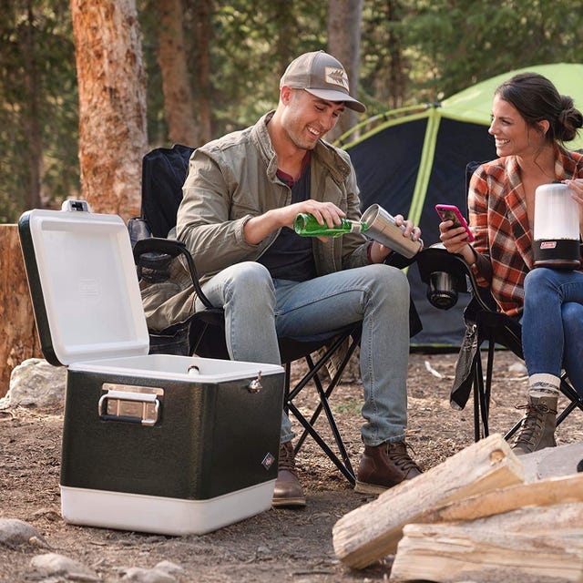 Coleman Steel-Belted 54-Quart Cooler a campsite with a cooler, logs, a couple in camping chairs and a tent