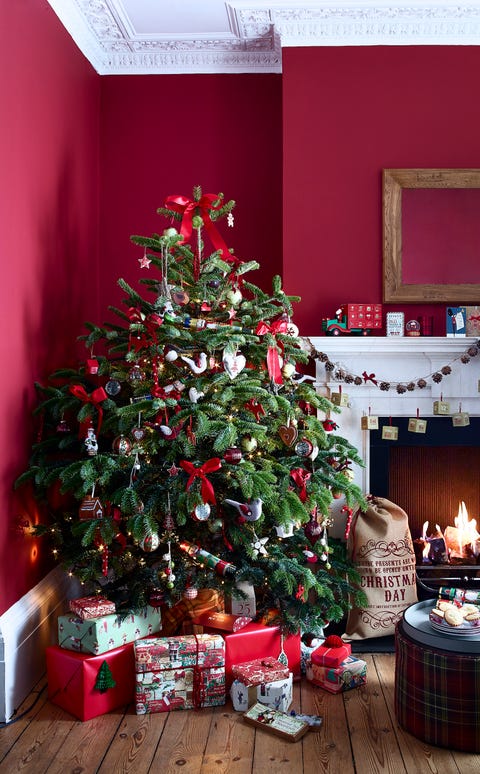 vibrant red living room with traditional cornicing and fireplace, lit fire, wooden floor, wrapped presents below decorated christmas tree in corner of room, decorations, garland, classic,