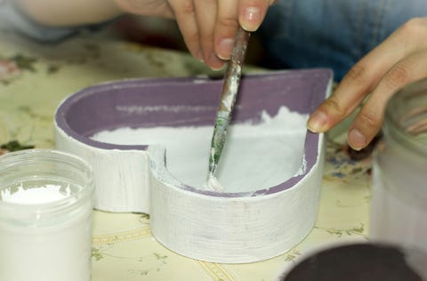 Mains peignant l'intérieur d'une boîte en bois en forme de coeur violet blanc