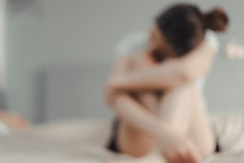 defocused image of sad woman sitting on bed at home