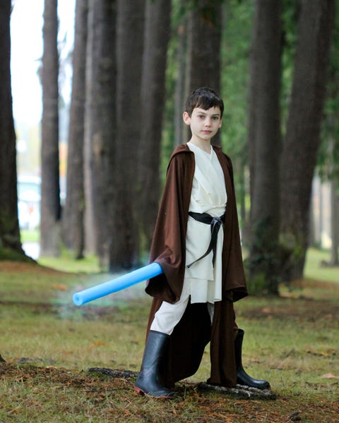 Boy standing outside dressed as Obi-Wan with blue pool noodle as light saber and long brown robe boy standing outside dressed as obi wan with blue pool noodle as light saber and long brown robe