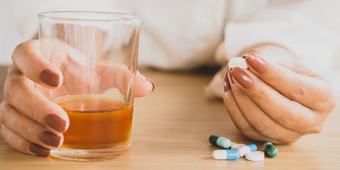 depressed woman hand taking overdose pills with glass of alcohol