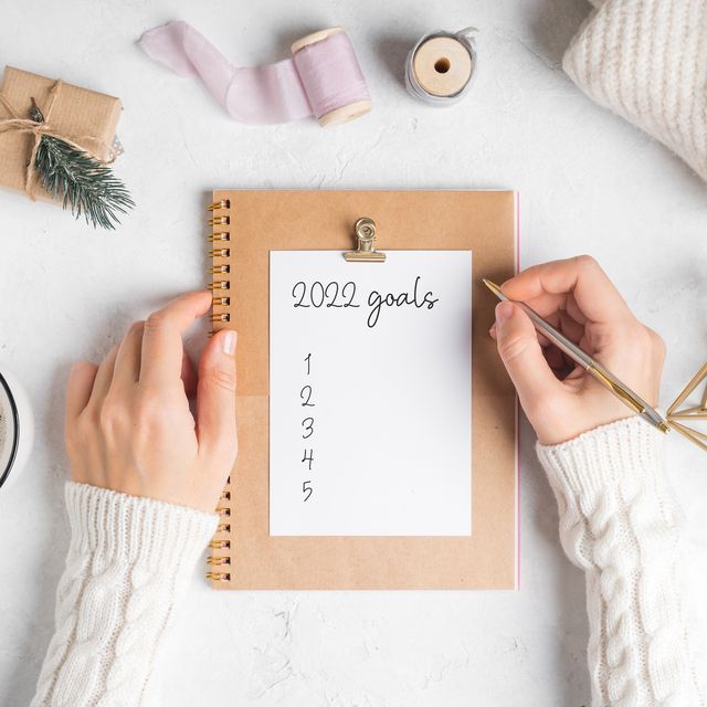 desktop of woman hands with blank notepad writing 2022 goals text  flat lay of white working table background with cup of coffee and christmas decoration top view mock up