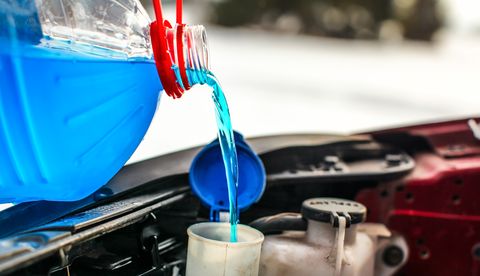Detail over het gieten van antivriesvloeistof ruitensproeiervloeistof in vuile auto uit blauwe en rode anti vries water container.