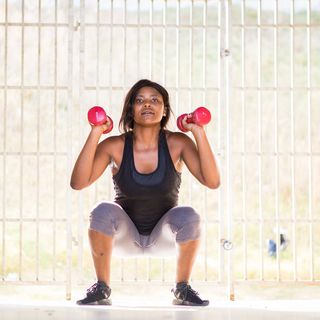 african american woman doing a squat exercise with dumbbells