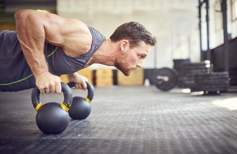 Determined athlete doing push-ups on kettlebells in gym