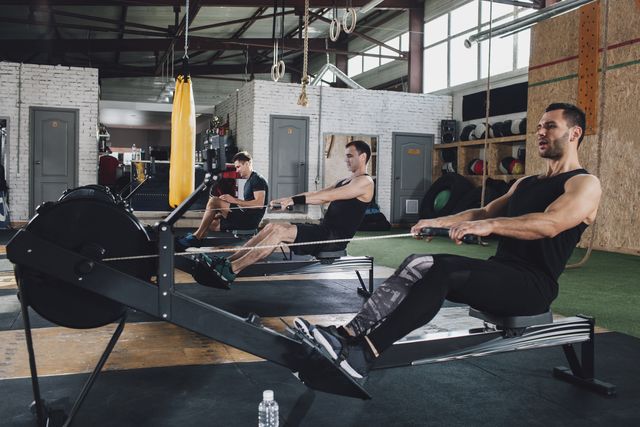 determined men exercising on rowing machines at health club