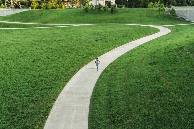 distant mixed race woman running on winding path in park