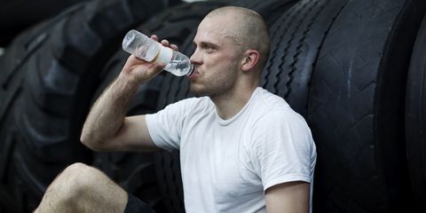 Man leaning on tires in gym center, drinking