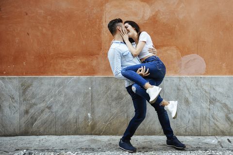 Carefree, affectionate couple in love in front of a wall outdoors.