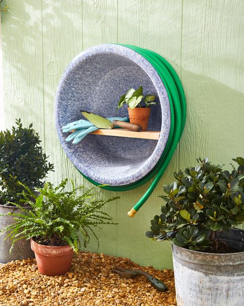 garden tools and hose catchall made from a vintage large enamelware pan hung on a green wall
