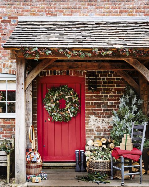 pub orig country house, red front door with assorted decorations, wreath, chair and basket with presents, christmas tree