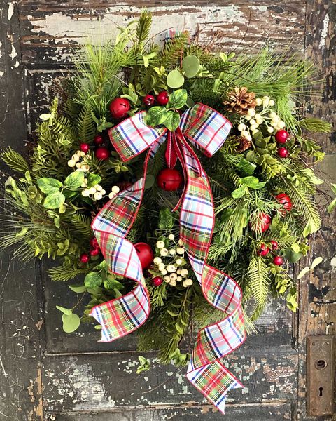 a greenery wreath with red  and white berries plus a large tartan bow