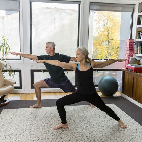 full length of couple with arms outstretched and legs apart exercising at home