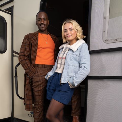 Doctor Who Stars Ncuti Gatwa und Millie Gibson in Kostümen am Set, die auf den Stufen eines Wohnwagens für ein First-Look-Foto posieren