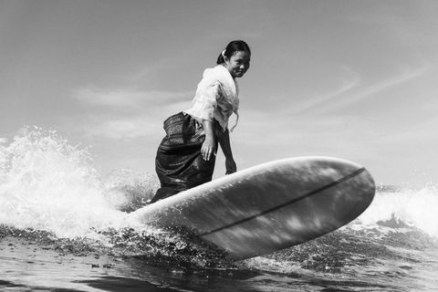 woman smiles while surfing in traditional clothes