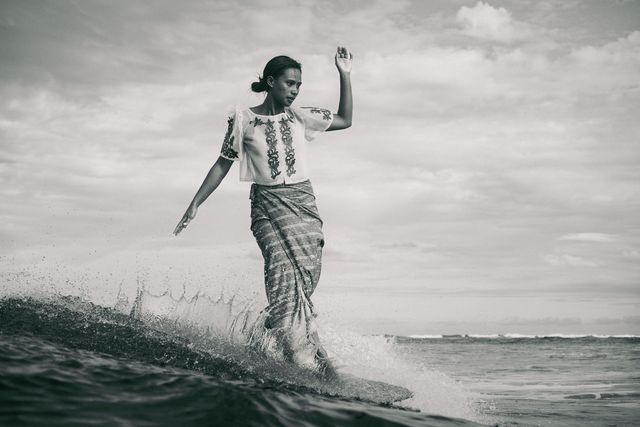 black and white photo of a woman dressed in traditional filipino clothes surfing