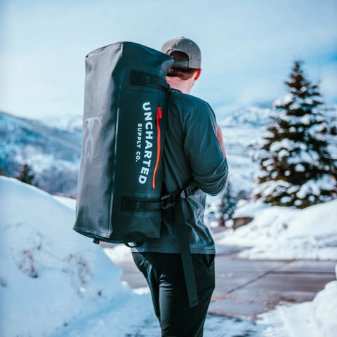 man carrying uncharted supply company the vault 65l duffel bag on his back walking in snow