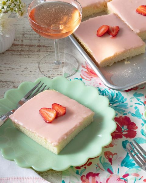 strawberries and rose sheet cake slice on green plate in front with glass of wine