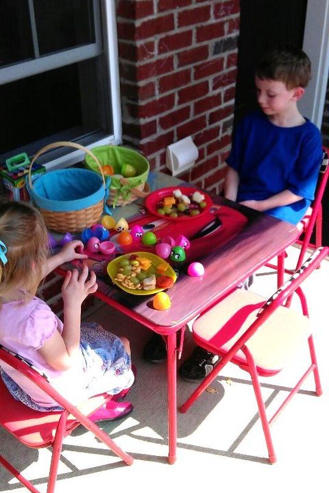 two children sitting at a red table eating lunch and playing with easter eggs