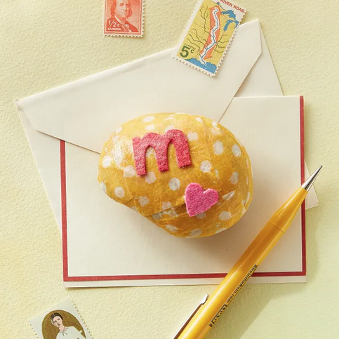 a small rock mod podged with yellow and white polkadot fabric topped with a letter "m" and small heart that have been cut out from felt