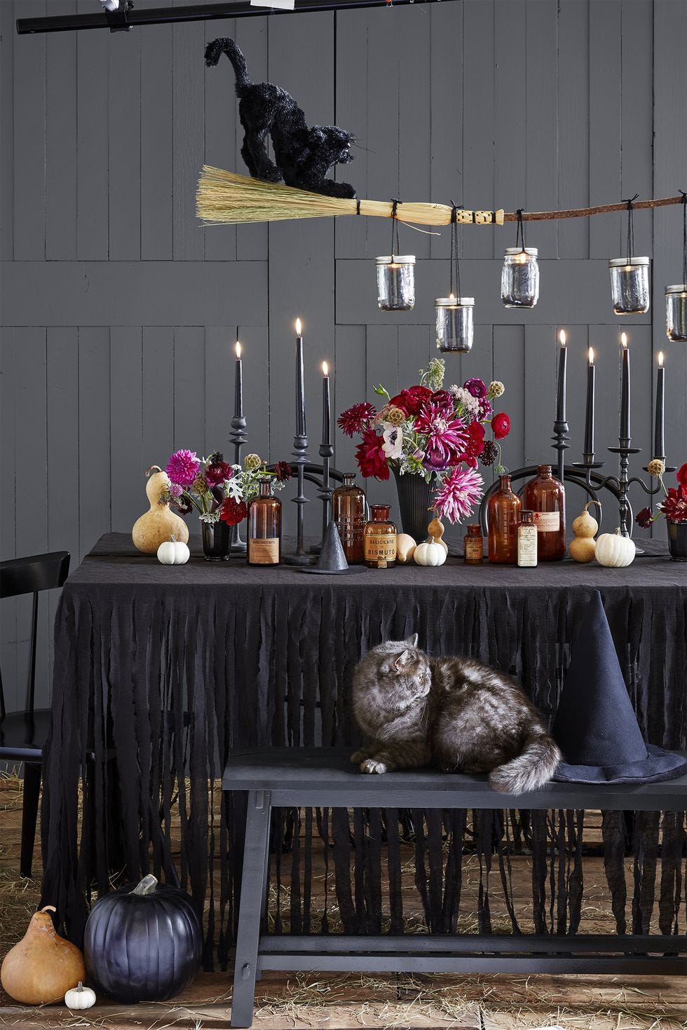 table display with black candles, pumpkins, amber jars, floral bouquets, and a broom with a black cat on top