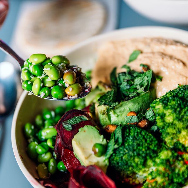 eating vegan bowl with edamame beans, broccoli, avocado, beetroot, hummus and nuts