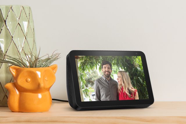 amazon echo show 8 on a table with a photo of a man and woman on the screen, next to a fox shaped orange plant pot