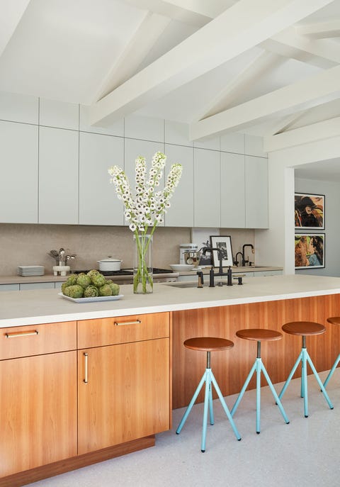 stark modern kitchen with an extra long island topped with a white counter and with wooden cabinets underneath and four simple turn screw stools pulled up to it