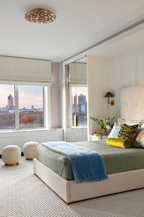 bedroom with a platform bed withwhite  tufted upholstered headboard green linens and a blue throw across it and like leopard print and floral print pillows and a gold bolster and two pouf in shirred white next to it