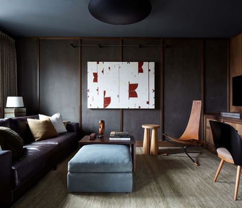 minimalist living space with dark brown leather sofa with a oblong velvet pouf beneath a small table in front a light washed stool and modern chairs a large white and red canvas sits in the center of the wall opposite