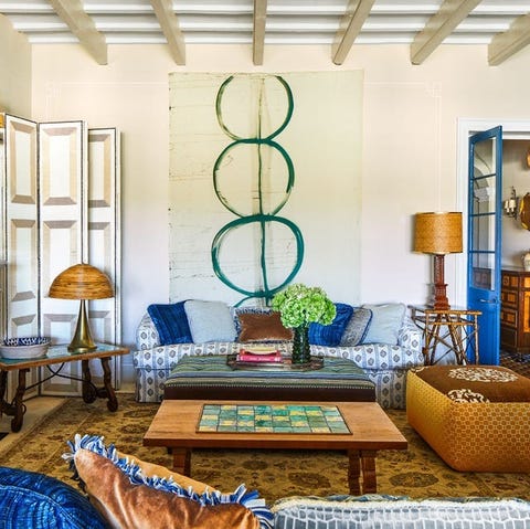 living area with blue and white sofa against the fa war and a game table at center and poufs and lamps on rattan and glass tables