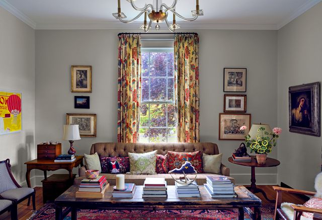living room with tall windows and curtains, sofa, and table piled with books